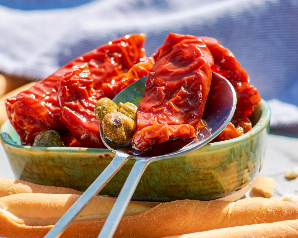 getrocknete Tomaten mit Kapern ein Schälchen mit getrockneten Tomaten, auf dem ein Löffel mit einer getrockneten Tomate und drei Kapern liegt